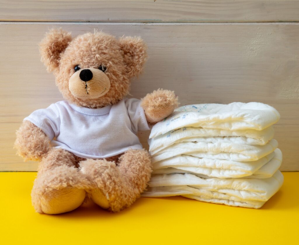 Baby diapers and teddy on yellow color floor