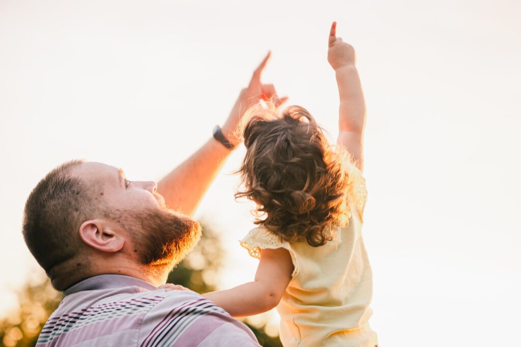 Daddy and daughter from behind looking up and showing finger on the sky