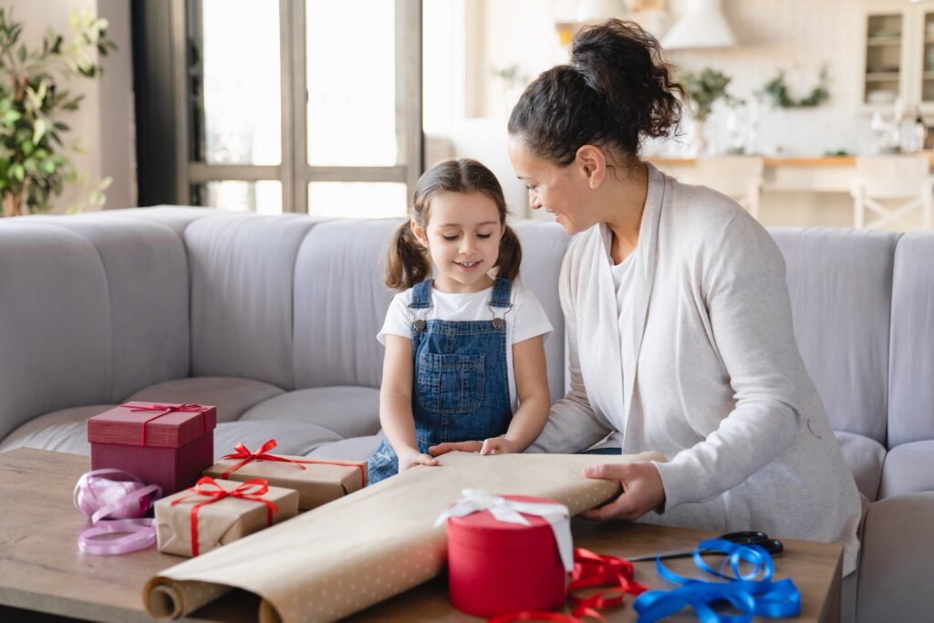 Daughter helping her mom with wrapping packing in paper birthday Christmas New Year presents gift
