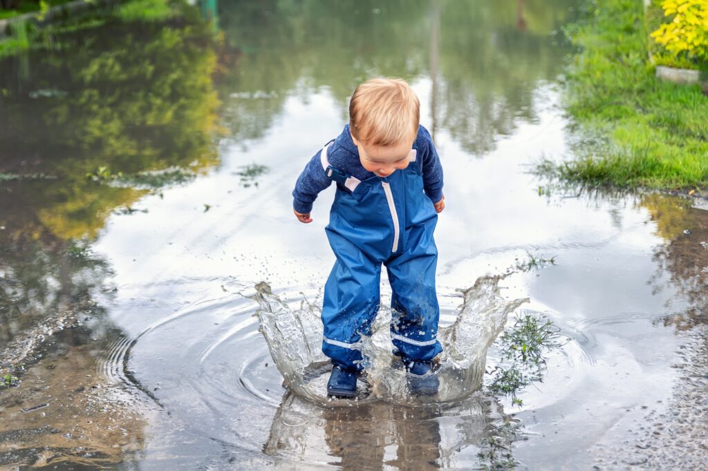 Little cute playful caucasian blond toddler boy enjoy have fun playing jumping in dirty puddle weari